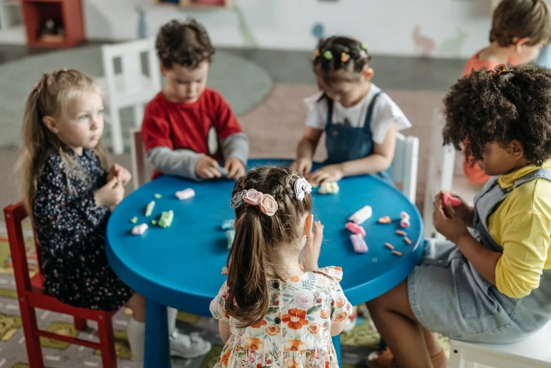 Sekelompok kecil anak bermain bersama di meja, didampingi terapis